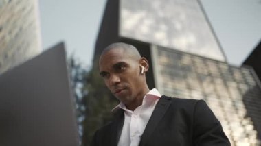 Kulaklıkla dışarıda dizüstü bilgisayarda çalışan güzel bir Afrikalı işadamı.