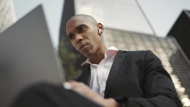 アフリカのビジネスマンがノートパソコンで仕事をしたり 屋外でヘッドフォンで話をしたり — ストック動画