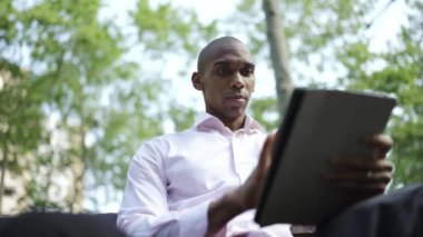 Serious African businessman typing by tablet in the park
