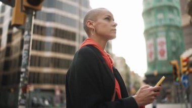 Ciddi kel bir kadın. Sokakta telefonla haritaya bakıyor.