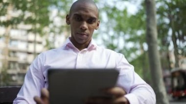 Pensive African businessman typing by tablet in the park
