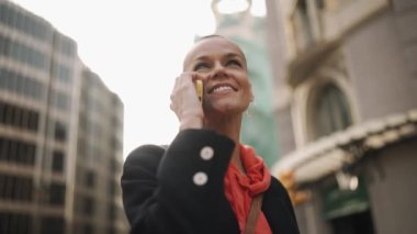 Smiling bald woman talking by mobile on the street