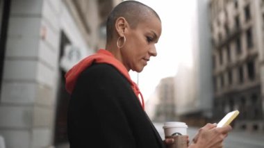 Ciddi kel bir kadın akıllı telefondan mesaj atıyor ve sokakta yürüyor.