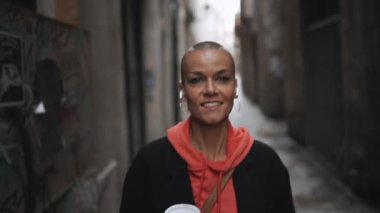 Yakışıklı kel kadın sokakta bir fincan kahveyle yürüyor.