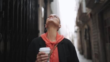 Güzel kel kadın sokakta bir fincan kahveyle yürüyor.