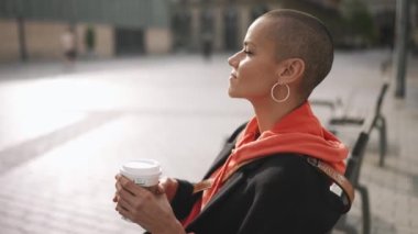 Meditasyon yapan kel kadın bankta kahve içiyor.