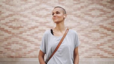 Tişört giyen neşeli kel kadın açık havada müzik dinliyor.