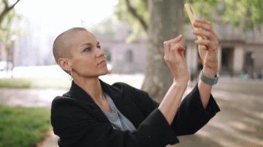 Yakışıklı kel kadın parktaki bankta telefonla video kaydediyor.