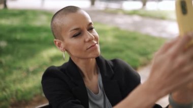 Güzel kel kadın parkta bankta telefonla video kaydediyor.