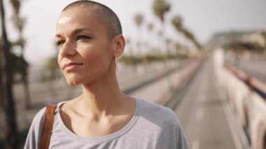 Gülümseyen kel kadın köprüde dururken kameraya bakıyor.