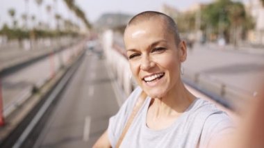 Gülümseyen kel kadın köprüde dururken video kaydediyor ve konuşuyor.