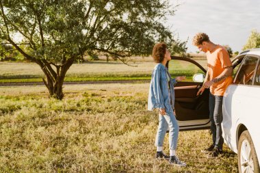 Genç, çok ırklı bir çift yaz gezisi boyunca konuşuyor ve arabada bekliyor.