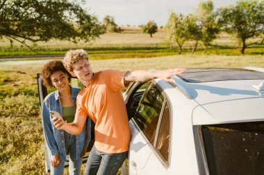 Genç, çok ırklı bir çift, araba yolculuğu sırasında cep telefonu kullanıyor ve elini uzatıyordu.