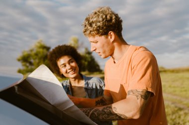 Genç çok ırklı çift araba gezisi sırasında konuşuyor ve haritayı inceliyor.