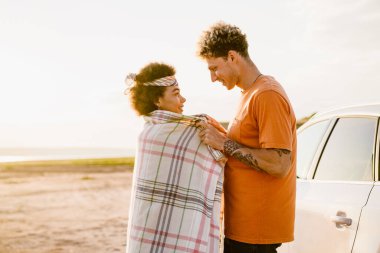 Araba gezisi sırasında gülümseyen ve birbirlerine bakan çok kültürlü genç bir çift.