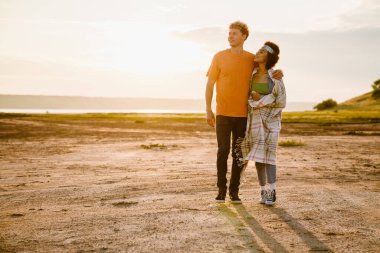 Genç, çok ırklı bir çift dışarıda yürürken sarılıp gülümsüyor.