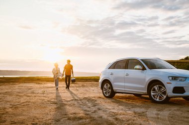 Genç, çok ırklı bir çift araba gezisi sırasında serin bir çantayla sahada dikiliyorlar.