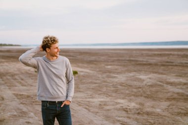 Genç beyaz adam dışarıda dururken gülümsüyor ve yan bakıyor.