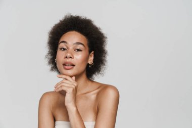 Siyah kıvırcık kadın beyaz arka planda yalnız poz veriyor ve kameraya bakıyor.