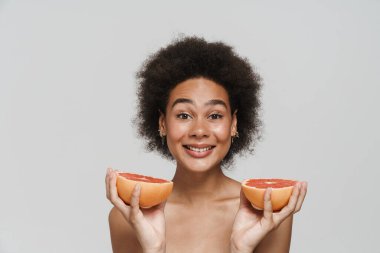 Beyaz arka planda izole edilmiş greyfurtla poz verirken gülümseyen siyah tişörtsüz kadın.