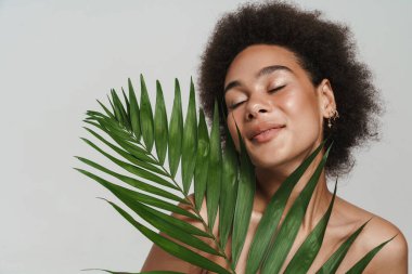Black shirtless woman smiling while posing with green leaf isolated over white background