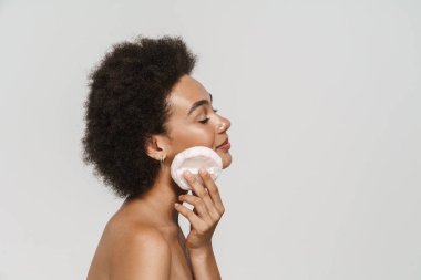 Beyaz arkaplanda izole edilmiş toz sünger kullanırken poz veren siyah kıvırcık gömlekli kadın.