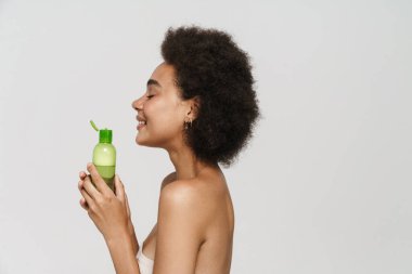 Siyah kıvırcık esmer kadın gülümserken beyaz arka planda izole edilmiş yüz losyonuyla poz veriyor.