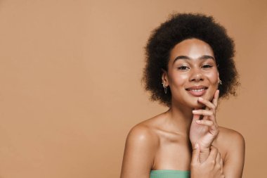 Siyah esmer kadın gülümsüyor ve bej arka planda izole edilmiş kameraya bakıyor.