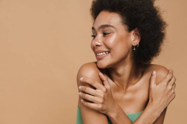 Siyah esmer kadın gülümsüyor ve bej arka planda izole edilmiş kameraya bakıyor.