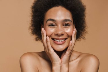 Siyah kıvırcık gömlekli kadın gülüyor ve bej arka planda izole edilmiş kameraya bakıyor.