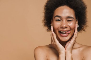 Siyah tişörtsüz kadın gülümsüyor ve bej arka planda izole edilmiş kameraya dilini gösteriyor.