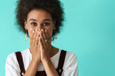 Mavi arka planda, ağzını kapatan siyah yüzükler takan genç bir kadın.