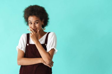 Küpeli siyahi bir kadın gülümsüyor ve mavi arka planda izole edilmiş kameraya bakıyor.