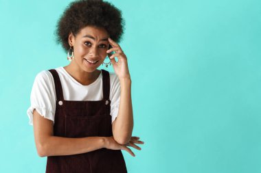 Küpe takan genç siyah kadın mavi arka planda izole edilmiş kameraya bakıyor ve gülümsüyor.