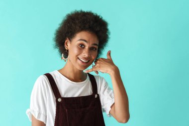 Küpeli siyahi genç bir kadın mavi arka planda izole edilmiş kamerada cep telefonu hareketi gösteriyor.