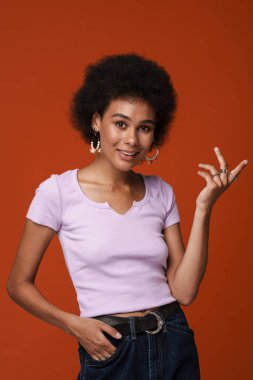 Kahverengi arka planda izole edilmiş siyah, küpe takan ve kameraya gülümseyen genç bir kadın.