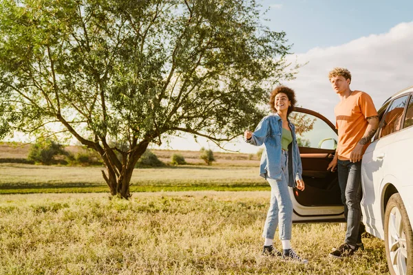 Genç, çok ırklı bir çift yaz gezisi boyunca konuşuyor ve arabada bekliyor.