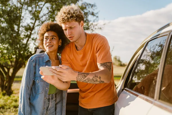 Genç, çok ırklı bir çift yaz gezisinde cep telefonu kullanıyor ve arabada bekliyor.