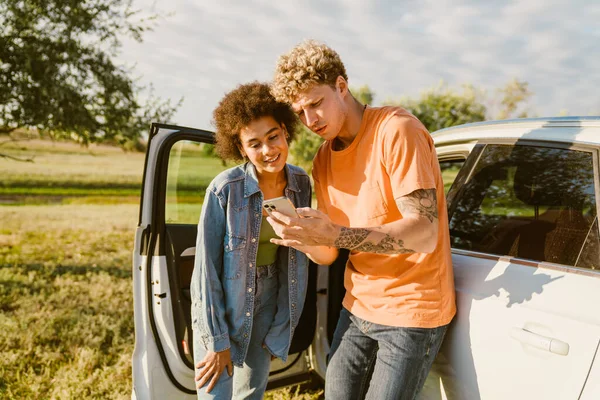 Genç, çok ırklı bir çift yaz gezisinde cep telefonu kullanıyor ve arabada bekliyor.