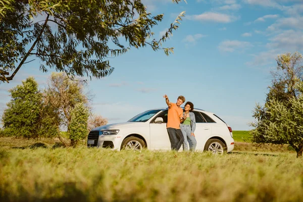 Genç, çok ırklı bir çift yaz gezisinde cep telefonu kullanıyor ve arabada bekliyor.