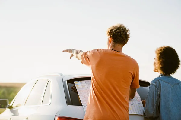 Young Multiracial Couple Examining Map Pointing Hand Away Car Trip —  Fotos de Stock