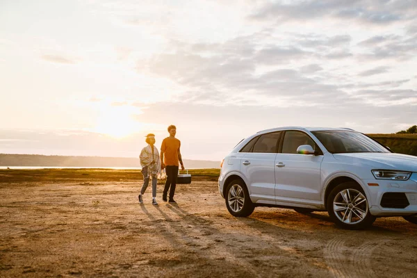 Genç, çok ırklı bir çift, serin çantalarla arabalarına biniyorlar.