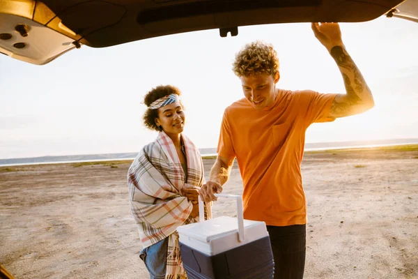 Young Multiracial Couple Putting Cooler Bag Trunk Car Trip — Stockfoto