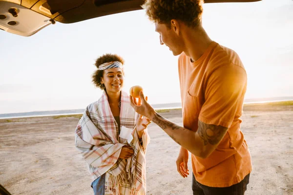 Genç, çok ırklı bir çift araba yolculuğunda bagajda beklerken şeftali yiyor.