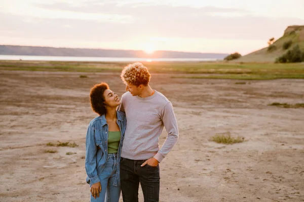 Genç, çok ırklı bir çift dışarıda yürürken sarılıp gülümsüyor.