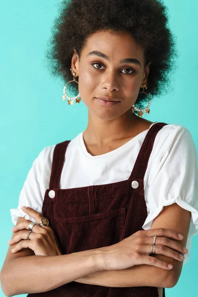 Küpe takan genç siyahi bir kadın mavi arka planda poz verip kameraya bakıyor.