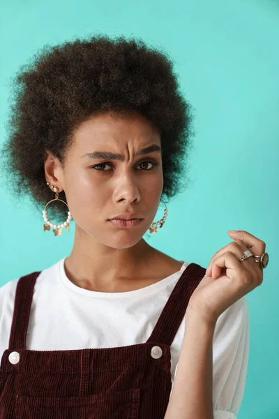 Küpe takan genç siyahi bir kadın mavi arka planda izole edilmiş kameraya bakıyor.