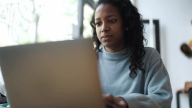 Kafede dizüstü bilgisayarla yazan mavi kazak giyen konsantre Afrikalı kadın.