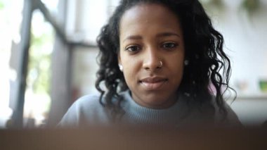 Cafe 'de dizüstü bilgisayarda yazan mavi kazak giyen yakışıklı Afrikalı kadın.