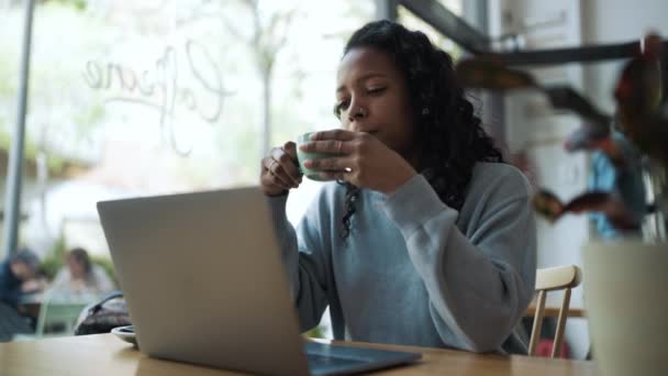 Pleased African Woman Wearing Blue Sweater Working Laptop Drinking Coffee — стокове відео